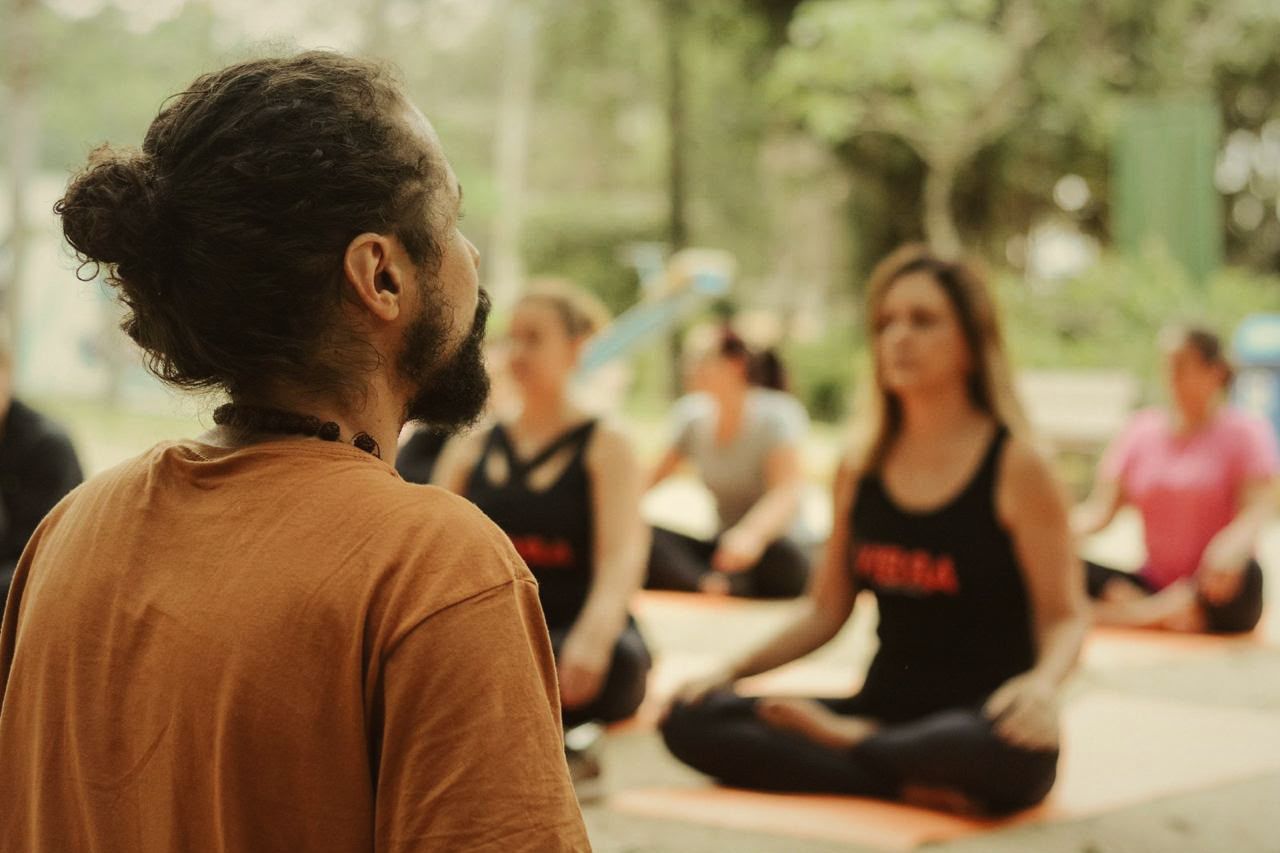 Douglas, de costas, conduz uma turma sentada em meditação ao ar livre